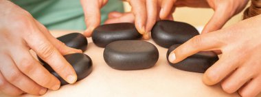 İki masaj terapisti kaplıcadaki kadına spa taşı takıyor.