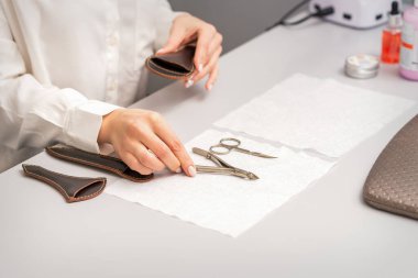 Manikürcünün elleri, manikür işlemleri için hazırlanan manikür aletlerini masaya bırakır.