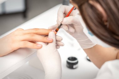 Manikür ustası kadın tırnaklarını saydam tırnak cilasıyla kaplıyor.