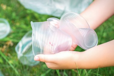 Çocuğun elleri çimlerdeki kullanılmış plastik çatal bıçaklardan parkı temizliyor.