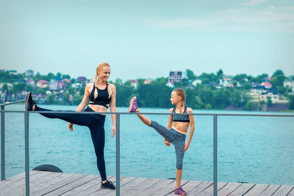 Kadın ve çocuk spor egzersizleri yapıyorlar. Rıhtımda bacaklarını açıyorlar. Gölde.