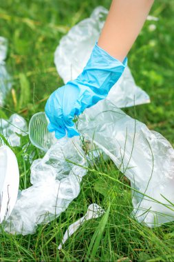 Çocuğun eli parktaki çimlerdeki plastik çatal bıçaklardan parkı temizliyor.