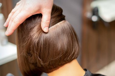 Kuaför kuaförde genç bir kadının kısa kahverengi saç modelini kontrol ediyor.