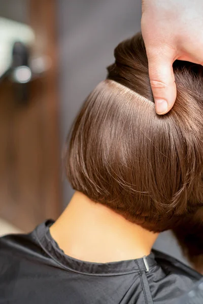 Hairdresser checks short brown hairstyle of a young woman in a beauty salon