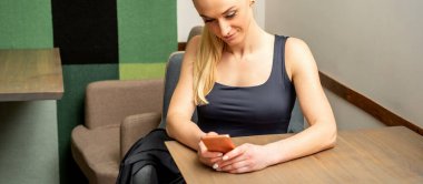 Kafedeki masada oturan akıllı telefona bakan güzel, beyaz bir kadın.