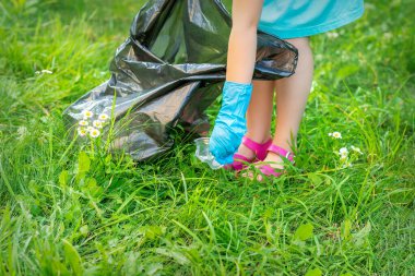 Çocuğun eli parktaki çimlerdeki plastik çatal bıçaklardan parkı temizliyor.