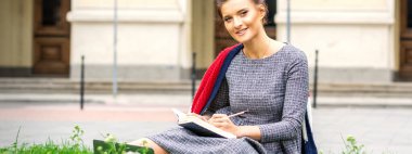 Üniversite binasının yakınındaki çimlerin üzerinde ders çalışan genç ve güzel bir öğrencinin portresi.