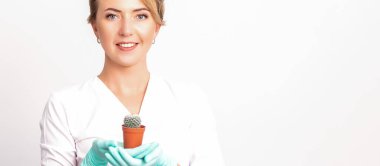 Genç, güzel, gülümseyen kadın güzellik uzmanı beyaz arka planda küçük bir kaktüs tutuyor.