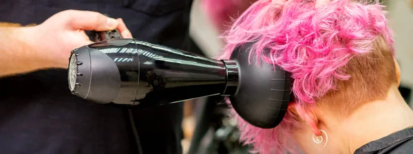 发型师在美容院里用吹风机吹干短粉色或红色头发的特写镜头 — 图库照片