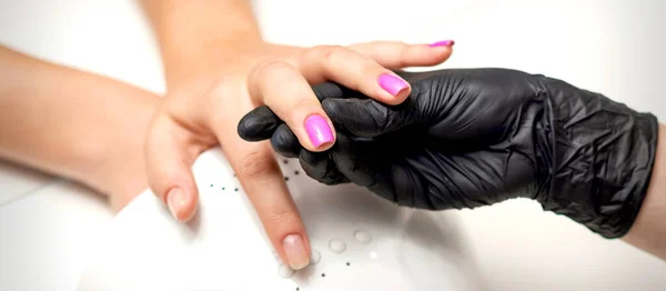 ネイルサロンで爪を描く間 マニキュアマスターの手は紫色のネイルポリッシュと女性の指を保持しています — ストック写真