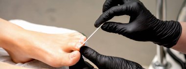Pedikür ustasının ellerinde koruyucu lastik eldivenler kadın tırnaklarını güzellik salonunda tırnak törpüsü ile törpülüyor.