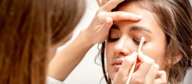 Makyöz, beyaz bir arka plana karşı güzel beyaz bir beyaz kadının gözüne göz farı sürüyor.