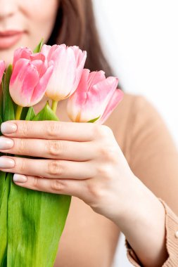 Beyaz bir arka planda pembe laleleri tutan beyaz bir kadın.