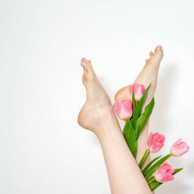 Güzel, ince, pürüzsüz bir kadının bacakları, beyaz arka planda laleler.