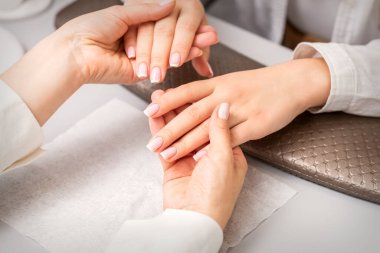 Manikür ustası, manikürcüde manikür yaptırmış genç bir kadının elini tutuyor.