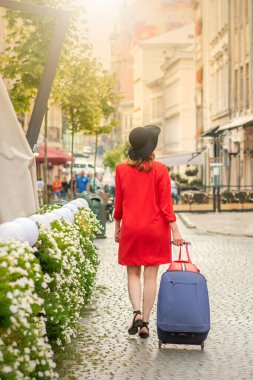Siyah şapkalı, bavullu genç bir kadın Avrupa caddesinde yürüyor.