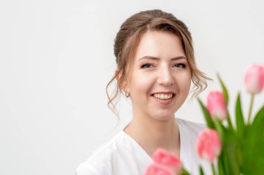 Beyaz arka planda pembe laleleri olan mutlu beyaz bir kadının portresi.