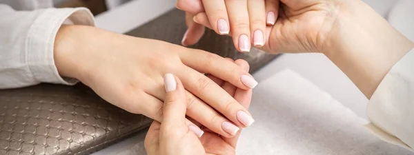 Manicure master holds hands of a young woman showing finished manicure on fingers in a nail salon