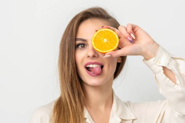 Gözünü portakal dilimiyle kaplayan ve dilini dışarı çıkaran neşeli beyaz bir kadının portresi beyaz arka planda beyaz gömlek giyer.