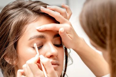 Makyöz, beyaz bir arka plana karşı güzel beyaz bir beyaz kadının gözüne göz farı sürüyor.