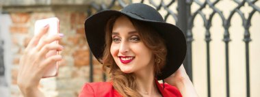Beautiful smiling caucasian young woman taking selfie on the smartphone against an urban background