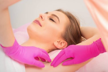 Kafkasyalı genç bir kadın, kuaför salonundaki güzellik uzmanının eldivenleriyle koltuk altlarına ağda yaptırıyor.