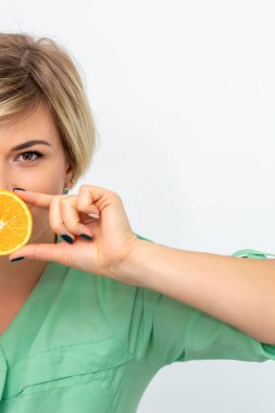 Half portrait of female dietitian holding and showing a slice of orange against her lips on a white background