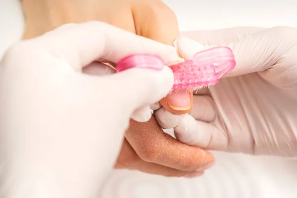 Closeup of manicurist is brushing dust with a pink plastic brush from female fingernails in a nail salon