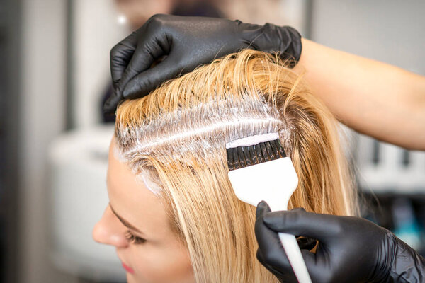 Парикмахер красил светлые корни волос щеткой для молодой женщины в парикмахерской