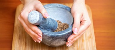 Kadın elleri ahşap mutfak tahtasındaki havanda kuru biber baharatlarını öğütür.