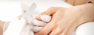 Manikür ustası, manikürcüde manikür yaparken tırnak törpüsü takıyor.