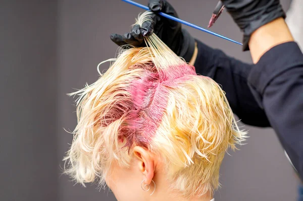 美发师的双手合拢 在美发店的金发女人的头发上涂上粉色染料 — 图库照片