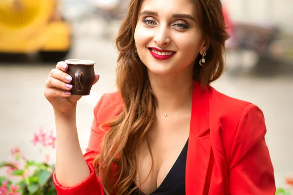 屋外のカフェでコーヒーを飲みながら座っているカメラを見ている美しい若い笑顔の白人女性の肖像画 — ストック写真