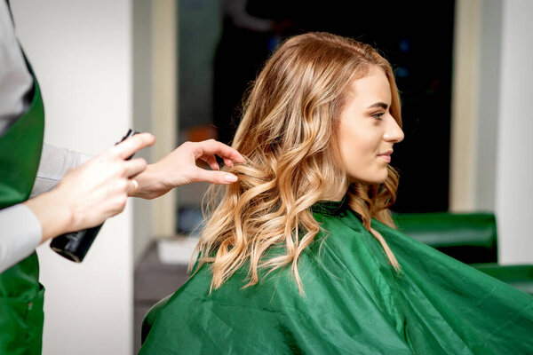 Side view of female hairdresser using hairspray fixing client's female hair in a hair salon