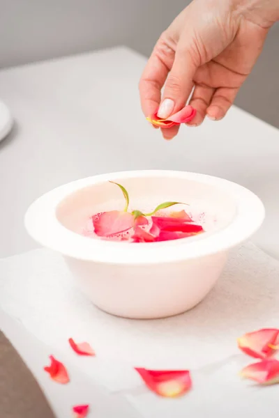 美容師の女性の手は スパでテーブルの上に赤とピンクのバラの花びらとマニキュアバスを準備 — ストック写真