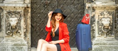 Siyah şapkalı, güzel, gülümseyen beyaz bir kadının portresi. Eski binada oturmuş dışarıdaki kameraya bakıyor.