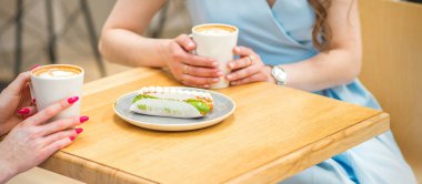 İki genç kadın kahve ve kek parçalarıyla açık bir kafede masada oturuyorlar.