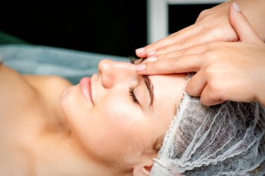 Kadın terapistin, spa güzellik salonundaki genç beyaz kadına alnı kırışıklıklarla dolu masaj yapan yan görüş parmakları.