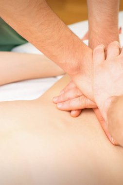 Bir kaplıca salonunda iki masör tarafından dört elle sırt masajı yapılan genç bir kadın.