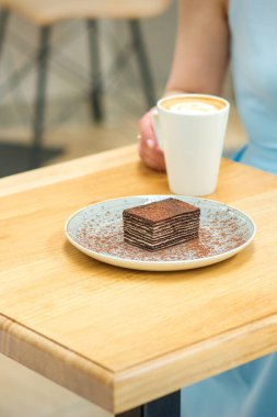 Bir fincan kahve ve kek ile genç bir kadın açık bir kafede masada oturuyor.