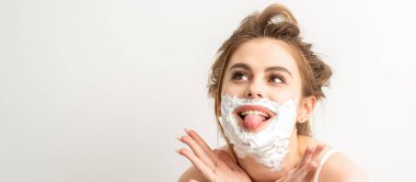 Yüzünde tıraş köpüğü olan güzel, genç, gülümseyen beyaz bir kadının portresi beyaz arka planda dilini dışarı çıkardı.