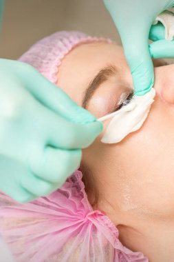 Kirpik temizleme prosedürü uygulanan genç bir kadın ve pamuklu bezle rimel temizler ve bir güzellik salonuna yapışır.