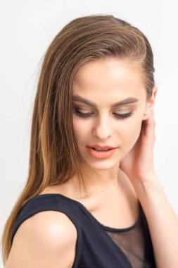 Doğal makyajlı, beyaz arka planda gülümseyen ve aşağı bakan güzel beyaz bir kadın.