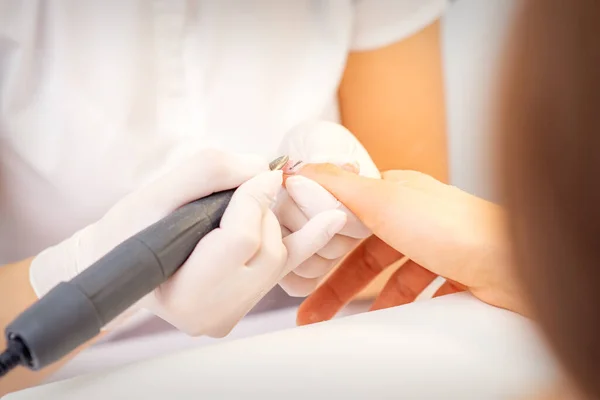 Closeup of manicure master in white gloves applying an electric nail file drill to remove the nail polish in the beauty salon
