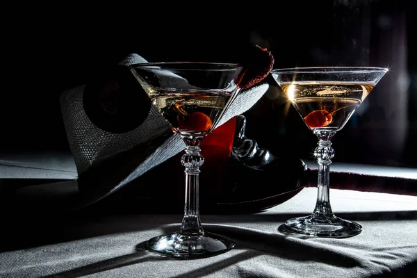 A couple of martini glasses with cherry and a cowboy hat on dark background