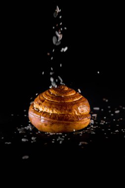 Tohumları siyah arkaplandan dökülen bir ekmek rulosu.