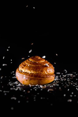 Tohumları siyah arkaplandan dökülen bir ekmek rulosu.