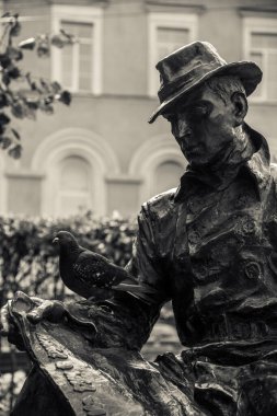 Etrafta güvercinlerle oturup kitap okuyan bir heykel.