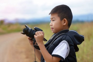 Genç bir çocuk dışarıda profesyonel bir kameraya bakıyor. Fotoğraf hobisi, öğrenme ve gelecekteki kariyer konsepti.                               