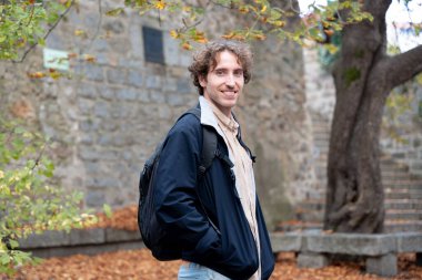 Genç bir adamın güz mevsiminde küçük bir kasabanın meydanında kameraya gülümsemesi.